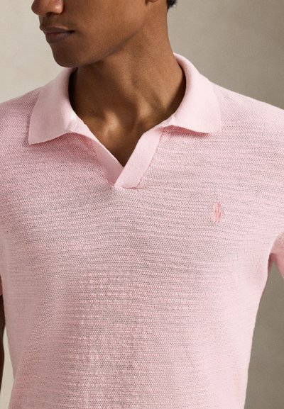 Πόλο μπλούζα με κοντό μανίκι και V-λαιμόκοψη σε ανοιχτό ροζ πλεκτό ύφασμα. Διαθέτει αντίθετο μαλακό γιακά και μικρό κεντημένο λογότυπο στο στήθος.