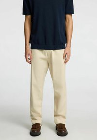 Marinblå kortärmad tröja, beige byxor, avslappnad passform, slät textur, få detaljer, i kombination med mörkbruna mockaskor.