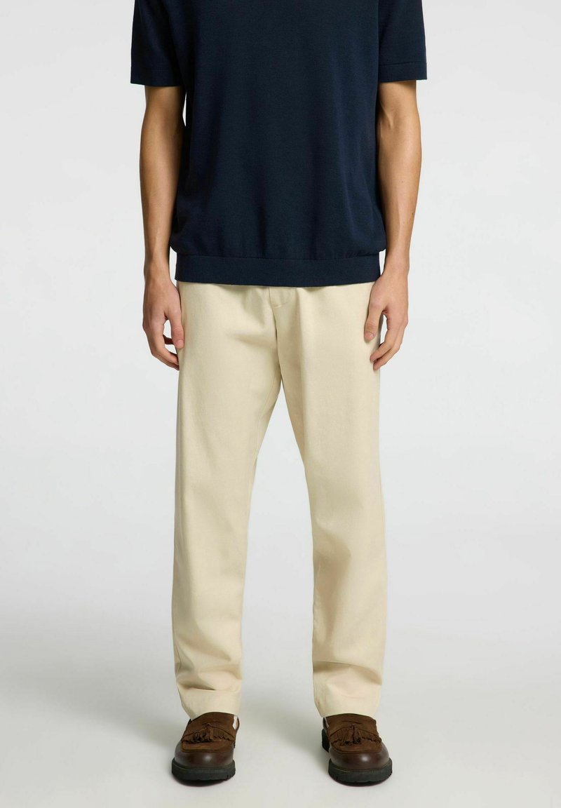 Marinblå kortärmad tröja, beige byxor, avslappnad passform, slät textur, få detaljer, i kombination med mörkbruna mockaskor.