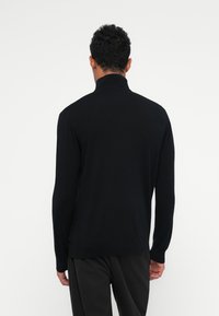 Schwarzer Strickpullover mit hohem Kragen, langen Ärmeln und glatter Textur. Verfügt über ein tailliertes Design und minimale Nähdetails.