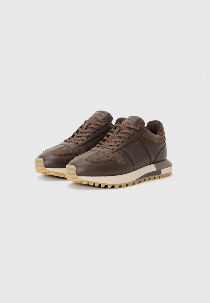 Bruine leren sneakers met geprofileerde bruine stofaccenten, een dikke crèmekleurige middenzool en een rubberen zool met een profielpatroon.