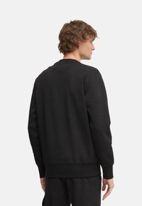 Sudadera negra hecha de tejido suave. Cuello redondo, mangas largas y puños acanalados. Diseño simple sin logotipos ni patrones visibles.
