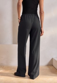 Pantaloni a gamba larga grigio scuro con elastico in vita e tasche laterali, realizzati in tessuto liscio con una sottile trama.