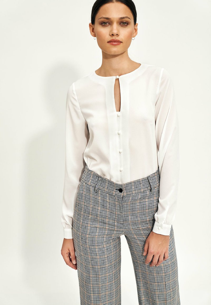 Biała bluzka z dekoltem w kształcie łezki i detalem w postaci guzików, w połączeniu z spodniami w kratkę o luźnym kroju i regulowanym pasku w talii.
