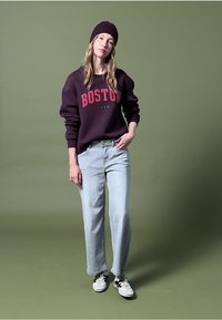 Sudadera color burdeos con la inscripción "BOSTON", jeans rectos de color azul claro y zapatillas negras y blancas. Combinado con un gorro a juego.