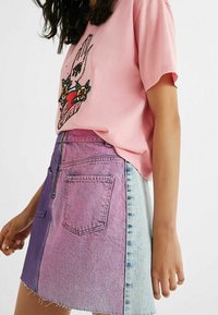 Camiseta de algodón rosa con estampado gráfico, combinada con una falda de mezclilla que presenta un degradado de púrpura a azul claro, con un dobladillo deshilachado.