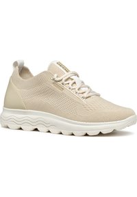 Sneaker in mesh beige con tomaia testurizzata, lacci elastici e suola bianca imbottita con design ondulato. Dettaglio del logo sulla linguetta.