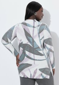 Długi sweter z długim rękawem z miękkiego materiału, ozdobiony dużym wzorem liści w odcieniach szarości, fioletu i niebieskiego z metalicznymi akcentami oraz ściągaczami przy rękawach.