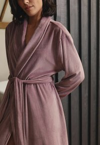 Rosa Cord-Velours-Robe mit Schalkragen, Gürtel und strukturiertem Stoff. Das Design hat lange Ärmel und einen lockeren Schnitt.