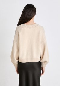 Beige knitted sweater with a loose fit, wide sleeves, and ribbed cuffs. The back features a crew neckline and a cropped hem.