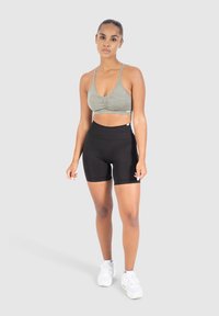 Oliivinvihreä urheiluvalu, jossa on rypytetty etuosasuunnittelu, yhdistettynä korkeavyötäröisiin mustiin shortseihin. Mallilla on päällä valkoiset urheilukengät.