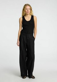 Black, sleeveless tank top with a geometric pattern, paired with high-waisted, wide-leg black trousers and open-toed black shoes.