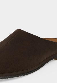 Σκούρο καφέ σουέντ παπούτσι τύπου slip-on με στρογγυλερή μύτη και μαύρη ελαστική σόλα, εμφανιζόμενο από πλευρική όψη με χαμηλή γωνία.