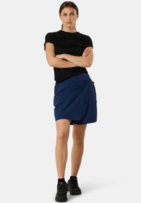 Navy blue skirt with a wrap-around design, made from lightweight fabric. Paired with a black t-shirt and black sneakers. Simple, modern look.