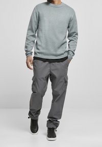 Světle modrý pletený svetr s žebrovanými manžetami, doplněný šedými cargo kalhotami s bočními kapsami a černými teniskami.