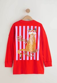 Chemise rouge à manches longues avec des rayures blanches verticales, avec un guépard portant des lunettes de soleil en forme d’étoiles et des hauts-de-forme, avec le texte scintillant "Sleigh Queen."