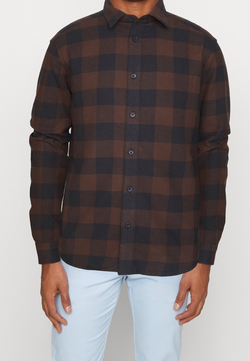 Bruine en zwarte geruite blouse met lange mouwen, knoopsluiting aan de voorkant en subtiele textuur. Voorzien van donkere knopen en een klassieke kraag.