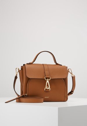 Sac à main DKNY en cuir marron avec poignée supérieure, rabat avant, fermeture dorée et bandoulière amovible sur un piédestal blanc.