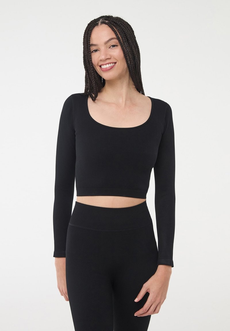 Czarny, długi rękaw crop top z szerokim dekoltem w kształcie łódkowym i prążkowaną teksturą, w połączeniu z wysokim stanem czarnych legginsów w tym samym stylu.