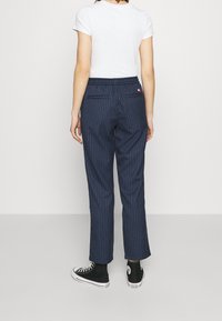 Granatowe spodnie w paski o luźnym kroju, z elastycznym paskiem w talii i dwiema tylnymi kieszeniami, zestawione z czarnymi sneakersami za kostkę.