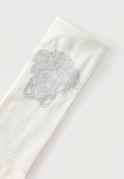 Chaussette blanche côtelée avec un motif de visage gris subtil près du bord supérieur sur fond blanc.