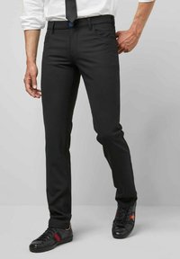 Zwarte op maat gemaakte broek van rekbaar materiaal, met een strakke vormgeving, voorzakken en een blauwe knoopaccent. Gekocht met zwarte sneakers.