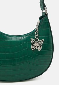 Grön faux läderaxelväska med krokodiltextur, med en silverfärgad fjäril charm fäst vid en kedja.