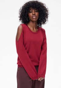 Bordowy sweter z długimi rękawami, z wycięciami na ramionach i prążkowanym dekoltem. Miękka tekstura o luźnym kroju.