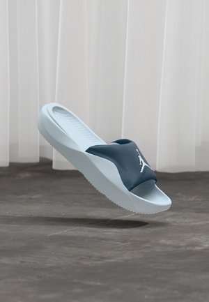 Blaue Rutschsandale mit einem Obermaterial aus Gummi, ausgestattet mit einem Logo, einer strukturierten Sohle und einer hellblauen Sohle. Glatte Oberfläche und offenes Design an der Zehe.