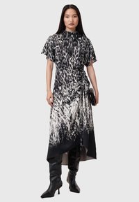 Vestido negro y blanco con estampado, de mangas cortas, con un dobladillo asimétrico y detalle fruncido en la cintura, combinado con botas negras hasta la rodilla.