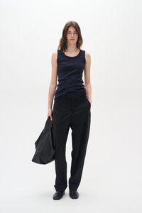 Mornarsko rebrasto majico, črne hlače visokega pasu, črna usnjena torba in črne čevlje, ki prikazujejo minimalistični, moderni estetski videz.