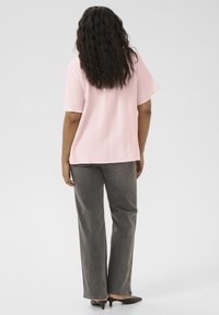 Top rose clair texturé à manches courtes associé à un pantalon droit gris et des talons noirs, vu de dos.