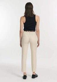 Beige Hose mit geradem Bein, getragen mit einem schwarzen Tanktop. Zu den Merkmalen gehören ein taillierter Bund und Hintertaschen. Schwarze Schuhe runden den Look ab.