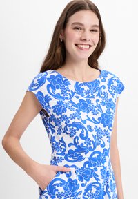 Floral-patterned dress with short sleeves, featuring bold blue designs on a white background and side pockets for functionality.