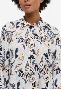Long-sleeve blouse in a lightweight fabric with a swirling pattern in navy, beige, and light blue. Features a button-down front and collar.