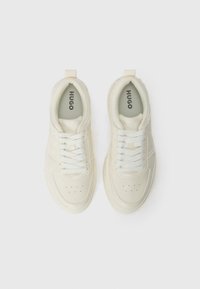 Hugo branded sneakers with a smooth, cream upper, rounded toe, lace-up closure, and a textured rubber sole.