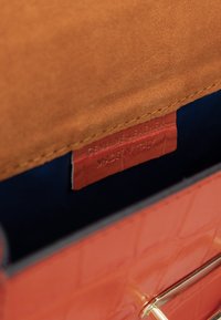 Indvendig i læderhandtasken med orange ægte læder med et struktureret mønster, brunt ruskindslining og en blå stoflomme.