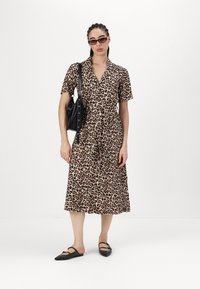 Lapių rašto midi suknelė su apykakle, trumpomis rankovėmis ir surišta juosmena. Dėvima su juodais aksesuarais ir plokščiomis bateliais.