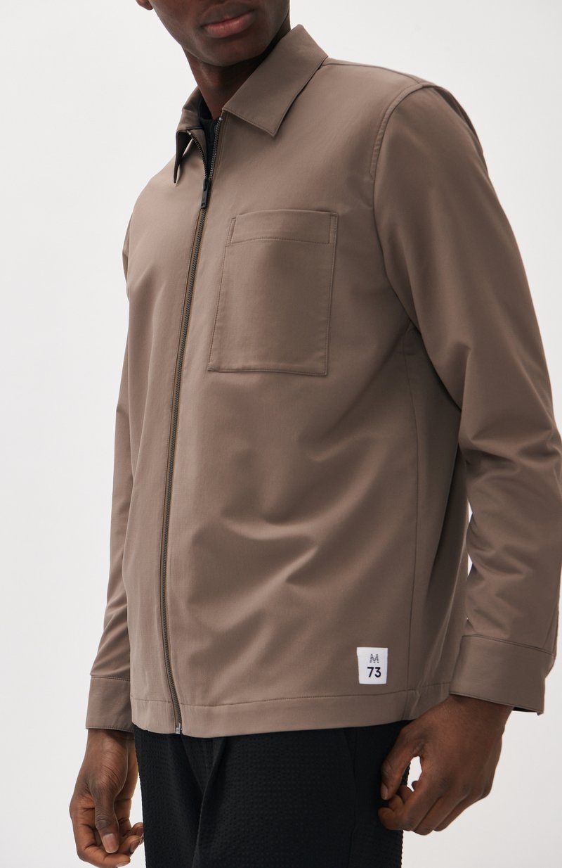 Veste zippée marron avec un col droit, poche poitrine unique, tissu texturé et étiquette logo à l'ourlet.