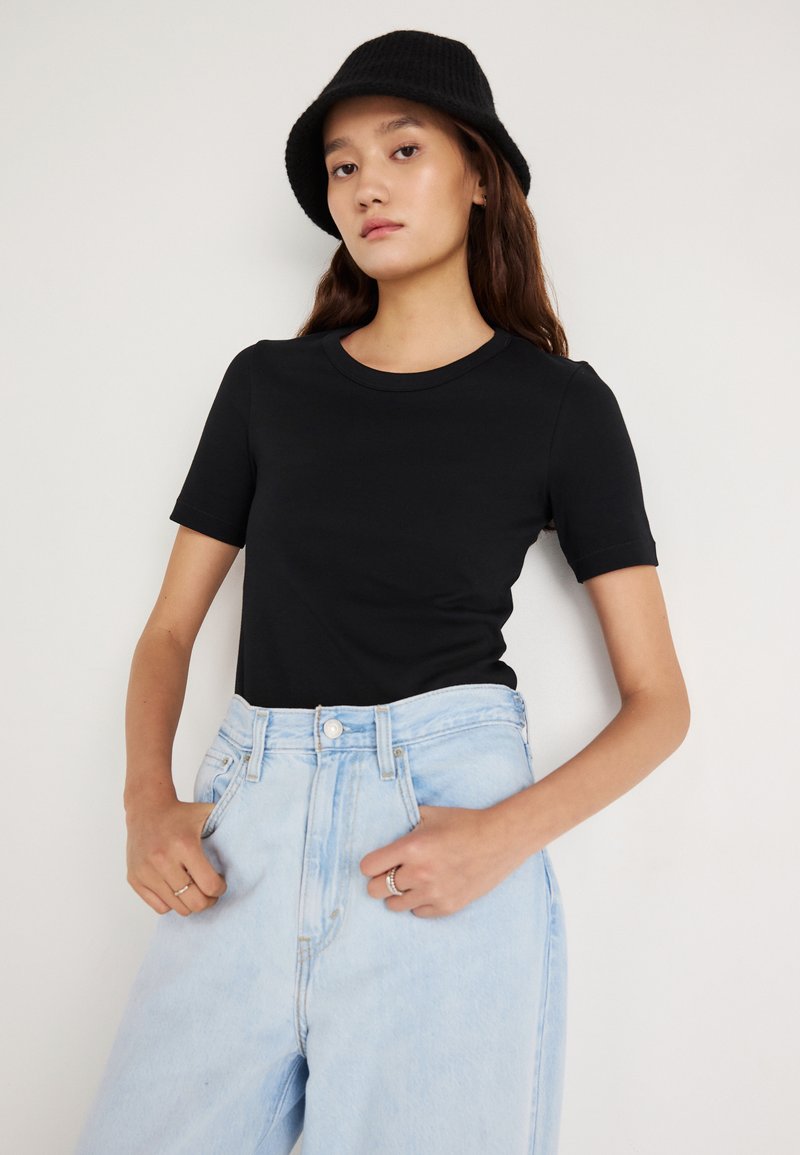 Černé tričko s krátkým rukávem z měkké látky, doplněné o vysoké světle modré denimové džíny. Charakteristické jsou kulatý výstřih a volný střih.