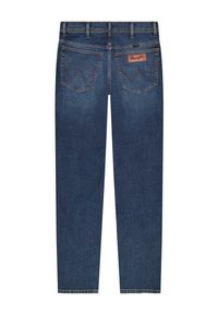 Σκούρο μπλε τζιν παντελόνι εμφανιζόμενο από πίσω, με δύο τσέπες με κέντημα σε σχήμα "W" και δερμάτινη ετικέτα της μάρκας Wrangler.