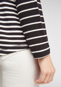 Pitkähihaista musta-valkoista raidallista paitaa, jossa on neulepinta, pyöreä helma ja kontrastivalkoiset tikkaukset hihojen reunoissa.