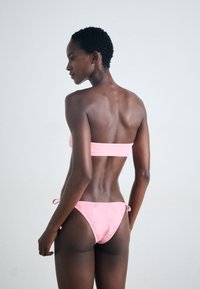Rosa bikini-set med et strapless topp og justerbare snøring-side underdeler. Materialet ser glatt ut med minimale sømmer og en tettsittende design.
