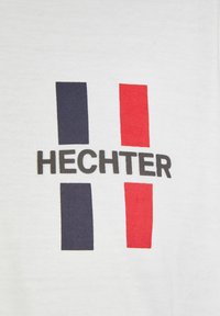 Witte katoenen T-shirt met de tekst "HECHTER" in zwart, met aan beide zijden verticale strepen in marineblauw en rood.