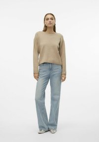 Pullover beige con una vestibilità comoda e scollo a girocollo, abbinato a jeans chiari a zampa d'elefante. Scarpe piatte argentate completano l'outfit.