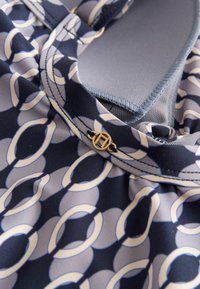 Gros plan sur un tissu bleu marine et gris clair avec un motif de chaîne circulaire et un petit bouton décoratif doré sur un col froncé.