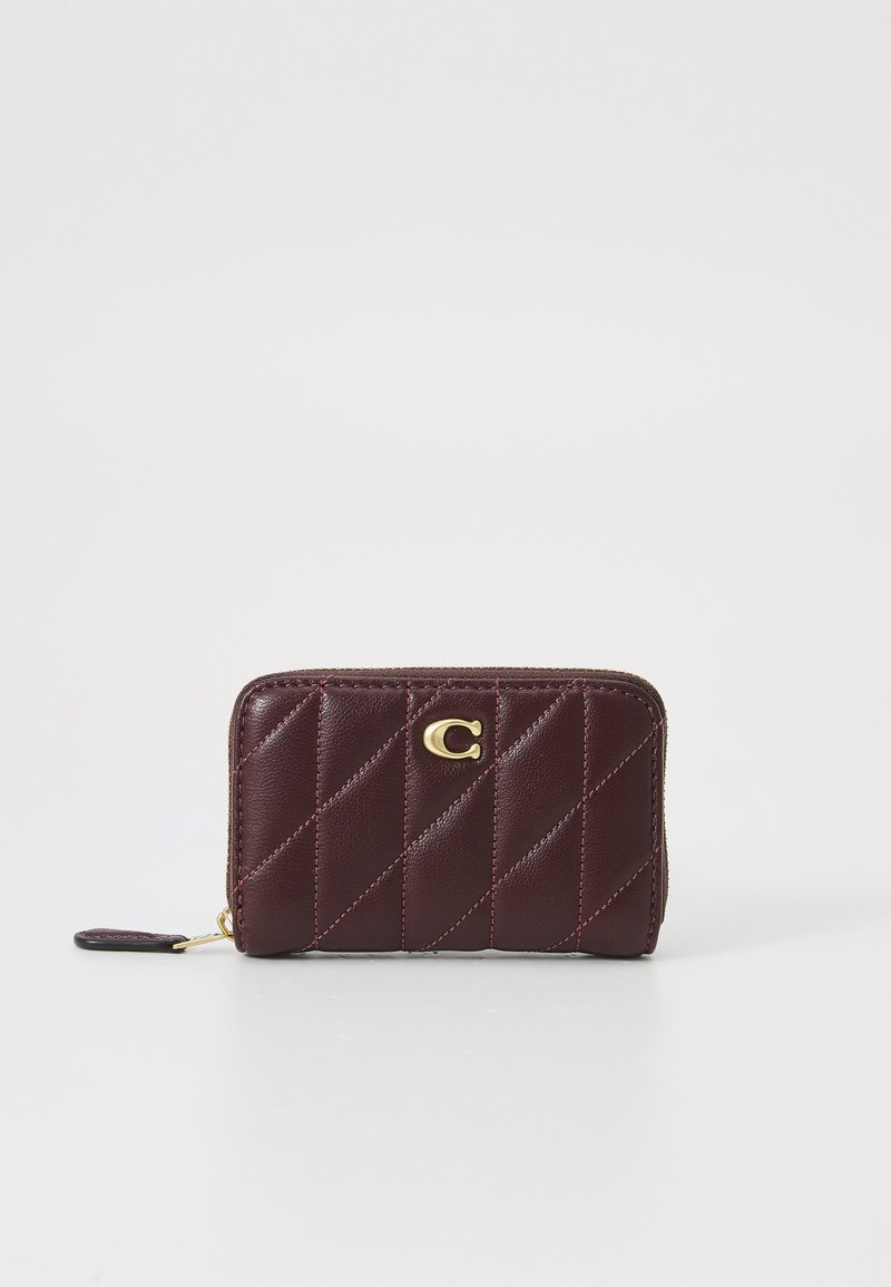 Portefeuille en cuir bordeaux avec un design matelassé, fermeture éclair et accent logo doré. Présente des coutures diagonales et une forme compacte.