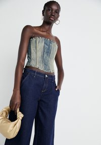 Denim top bez ramínek s vertikálními švy, v kombinaci s baggy tmavě modrými džíny a zlatou kabelkou přes rameno. Obsahuje kruhové náušnice.