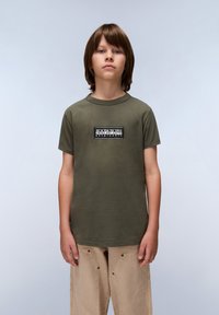 Olivegrünes Baumwoll-T-Shirt mit kurzen Ärmeln, rundem Ausschnitt und Logo-Patch auf der Vorderseite mit schwarz-weißem Text. Lockerer Schnitt.