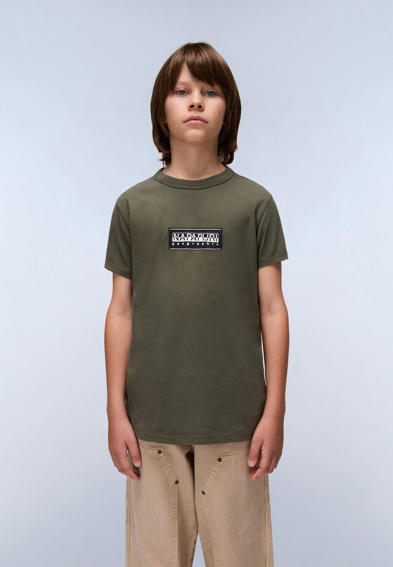 Olivegrünes Baumwoll-T-Shirt mit kurzen Ärmeln, rundem Ausschnitt und Logo-Patch auf der Vorderseite mit schwarz-weißem Text. Lockerer Schnitt.